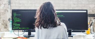 Female programmer sitting in front of two computer screens