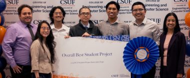 A group of smiling young people pose for a celebratory photo while holding a large banner that reads, “Overall Best Student Project” and a large blue ribbon.